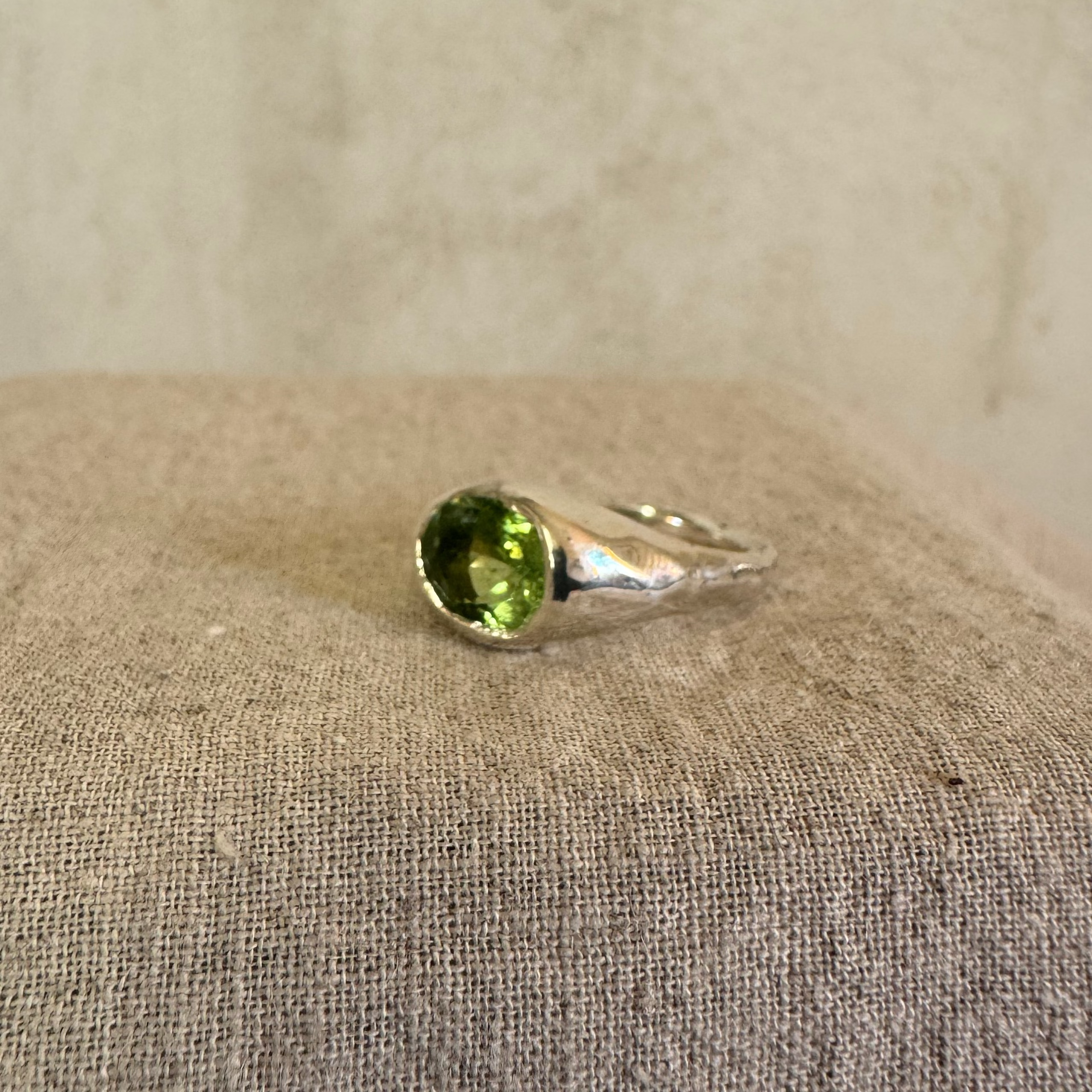 Silver ring with a green gemstone on a beige fabric background