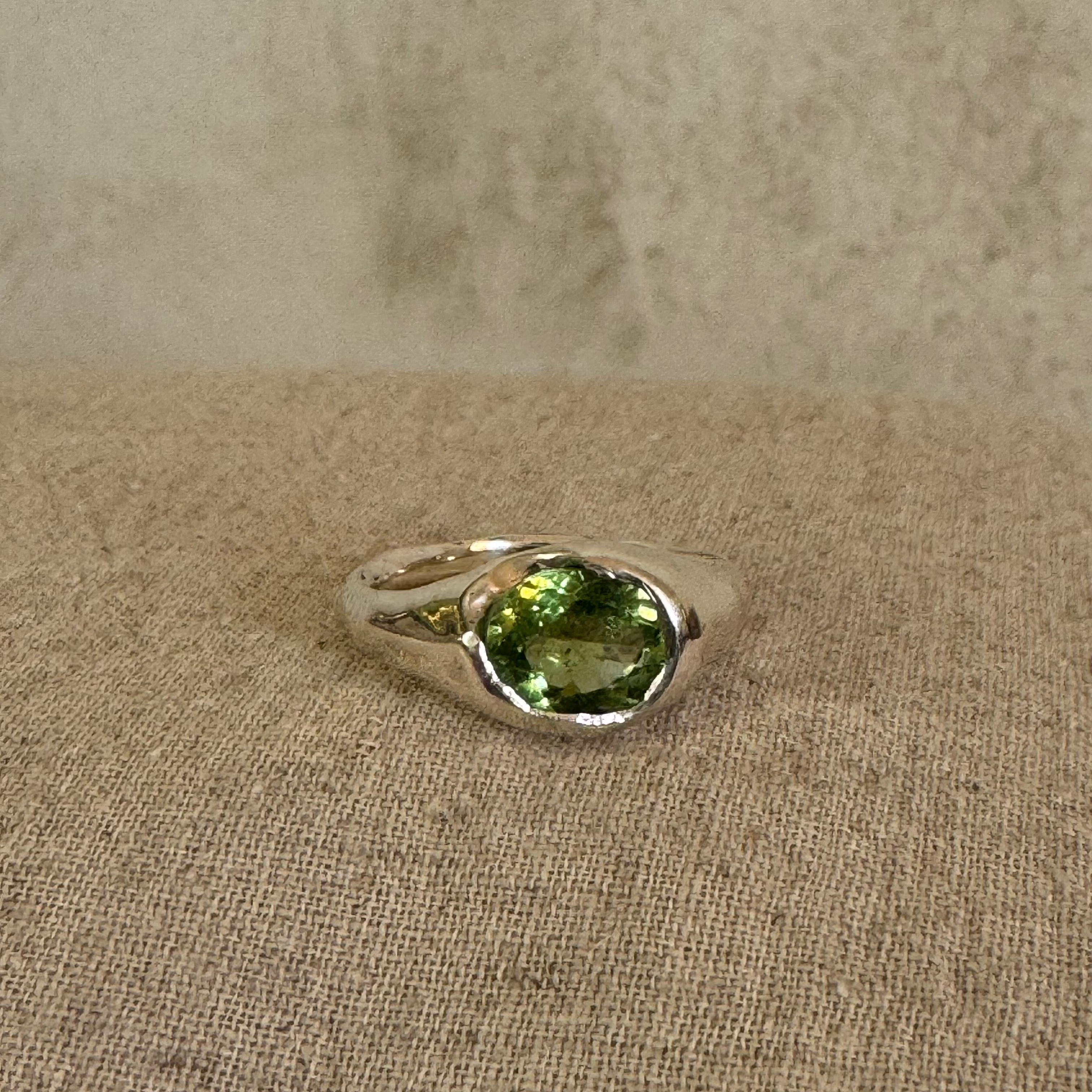 Silver signet ring with a green tourmaline gemstone on a linen fabric background