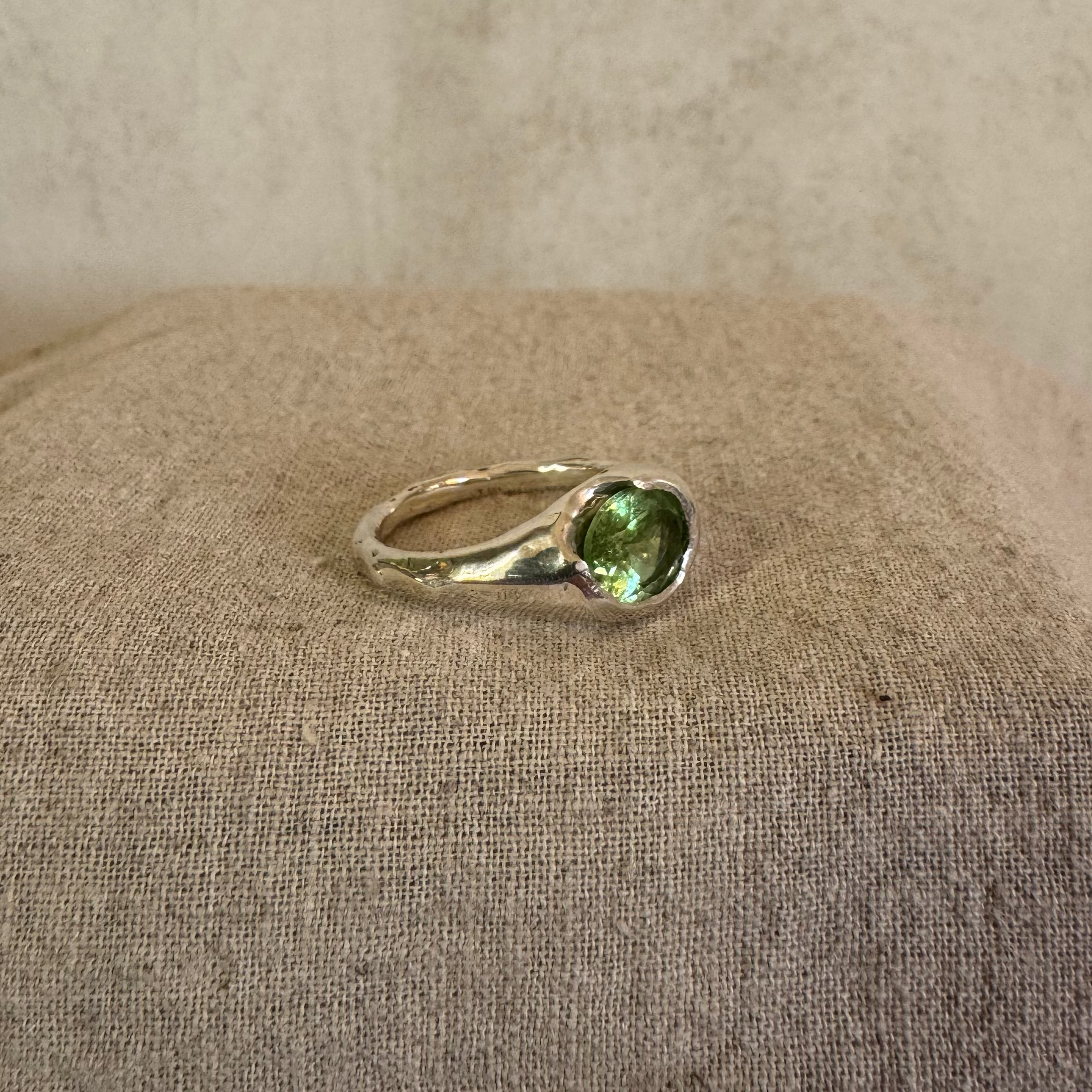 Organic silver ring with a green tourmaline gemstone on a linen fabric background