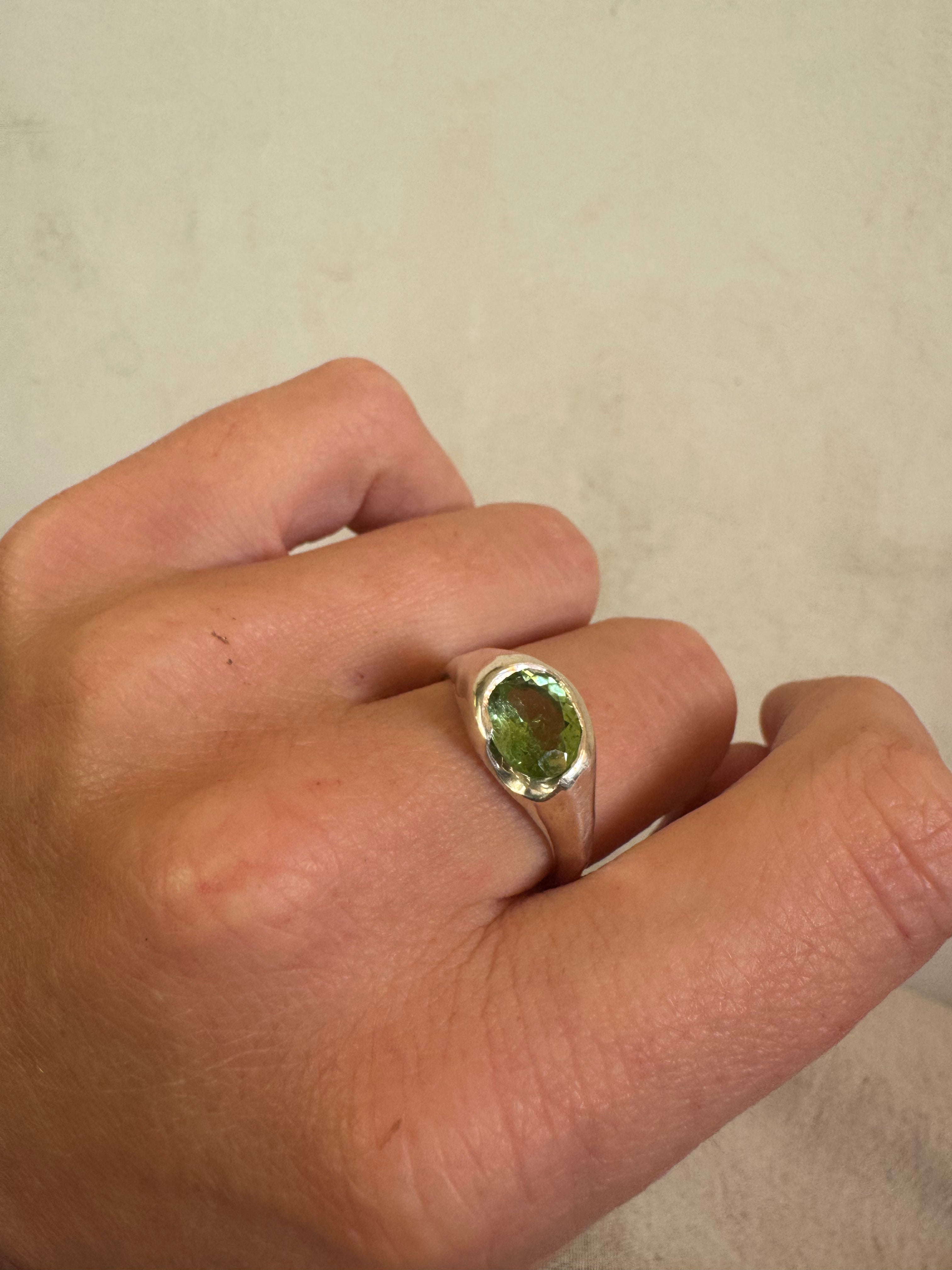 Hand wearing a ring with a green tourmaline gemstone on a plain background